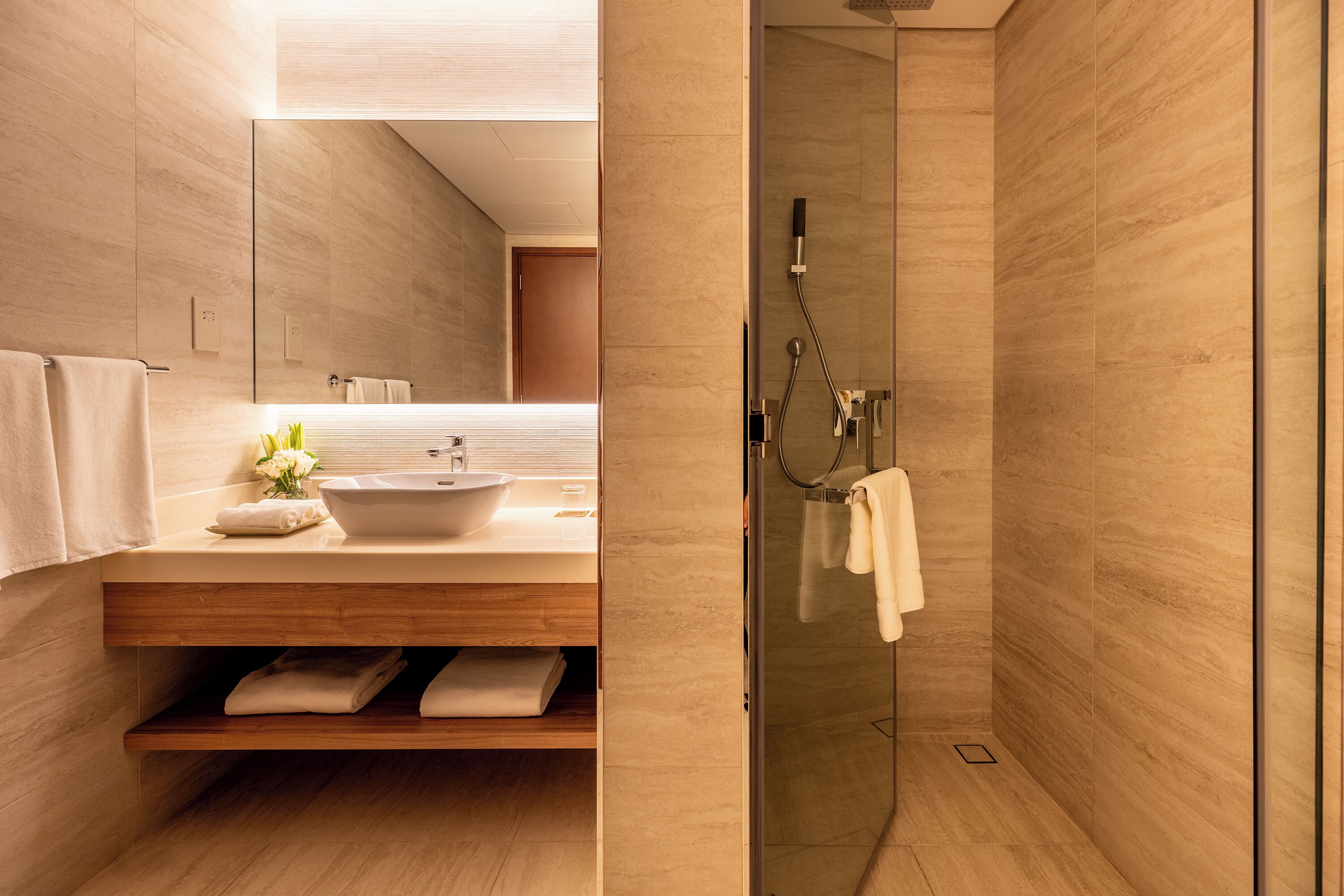 Un baño moderno con tocador de madera, cabina de ducha de vidrio y un espejo grande.
