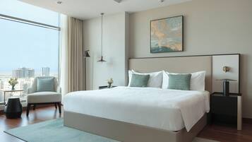 A modern hotel room with a large bed, a view of the city, a side table with a lamp, and a chair.
