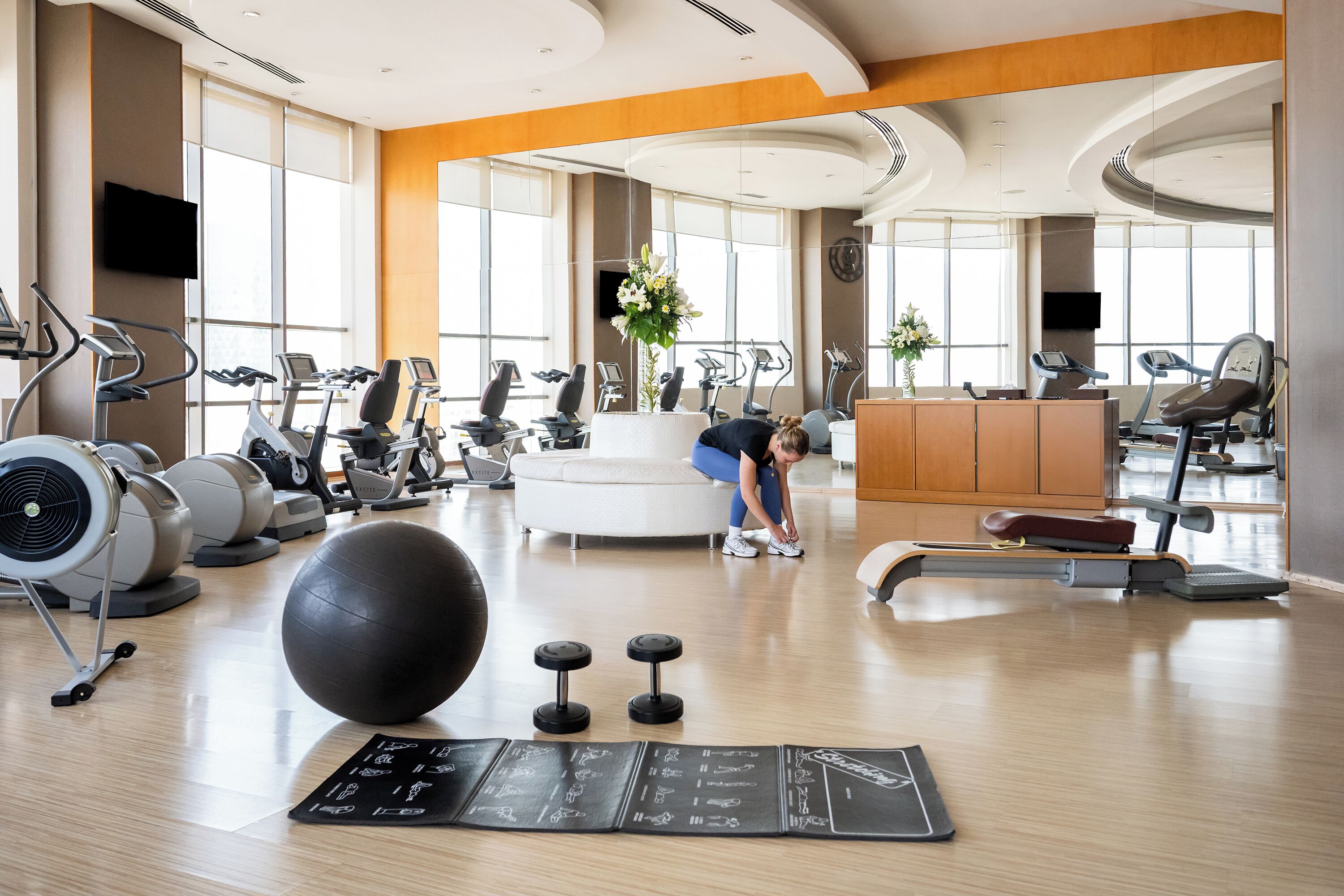 A gym with exercise equipment, a large exercise ball, dumbbells, and a mat with workout illustrations.
