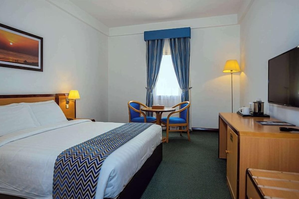 Habitación de hotel con cama, escritorio, silla, televisor y un cuadro en la pared.