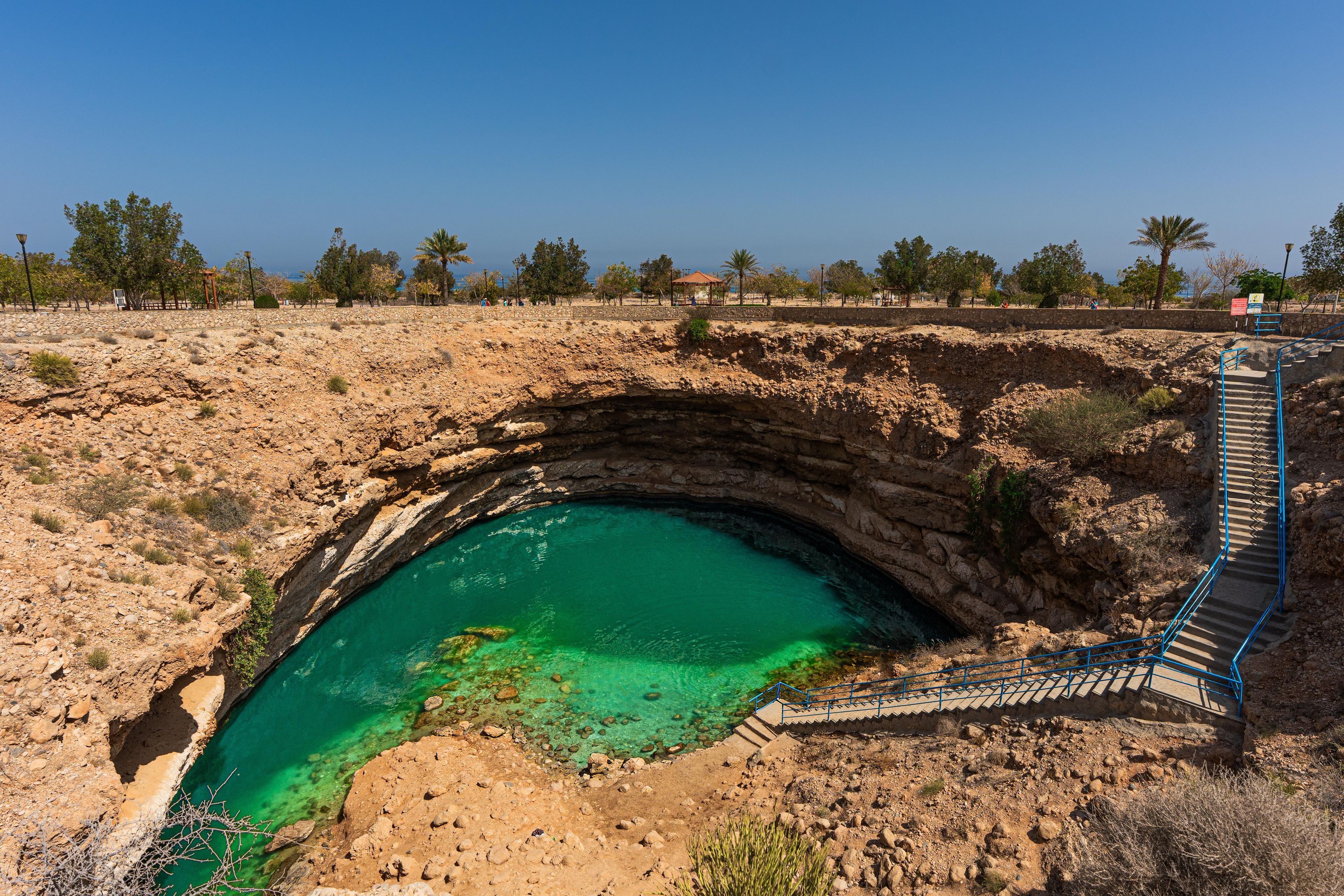 A natural pool with a stone bridge leading to a gazebo.