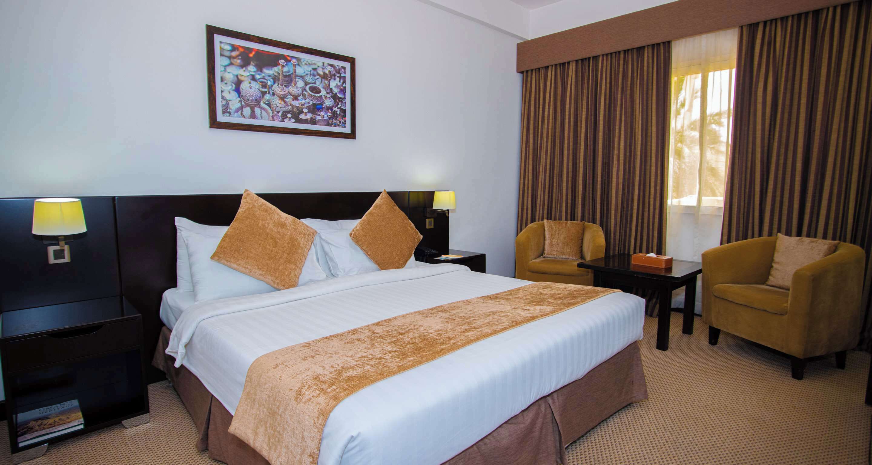A hotel room with a large bed, two nightstands, a desk, a chair, and a window with curtains.
