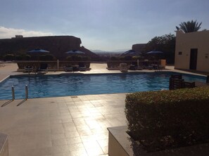 A swimming pool with lounge chairs and umbrellas, surrounded by a landscaped area with a view of distant mountains. - Best Western Sur (Sur)