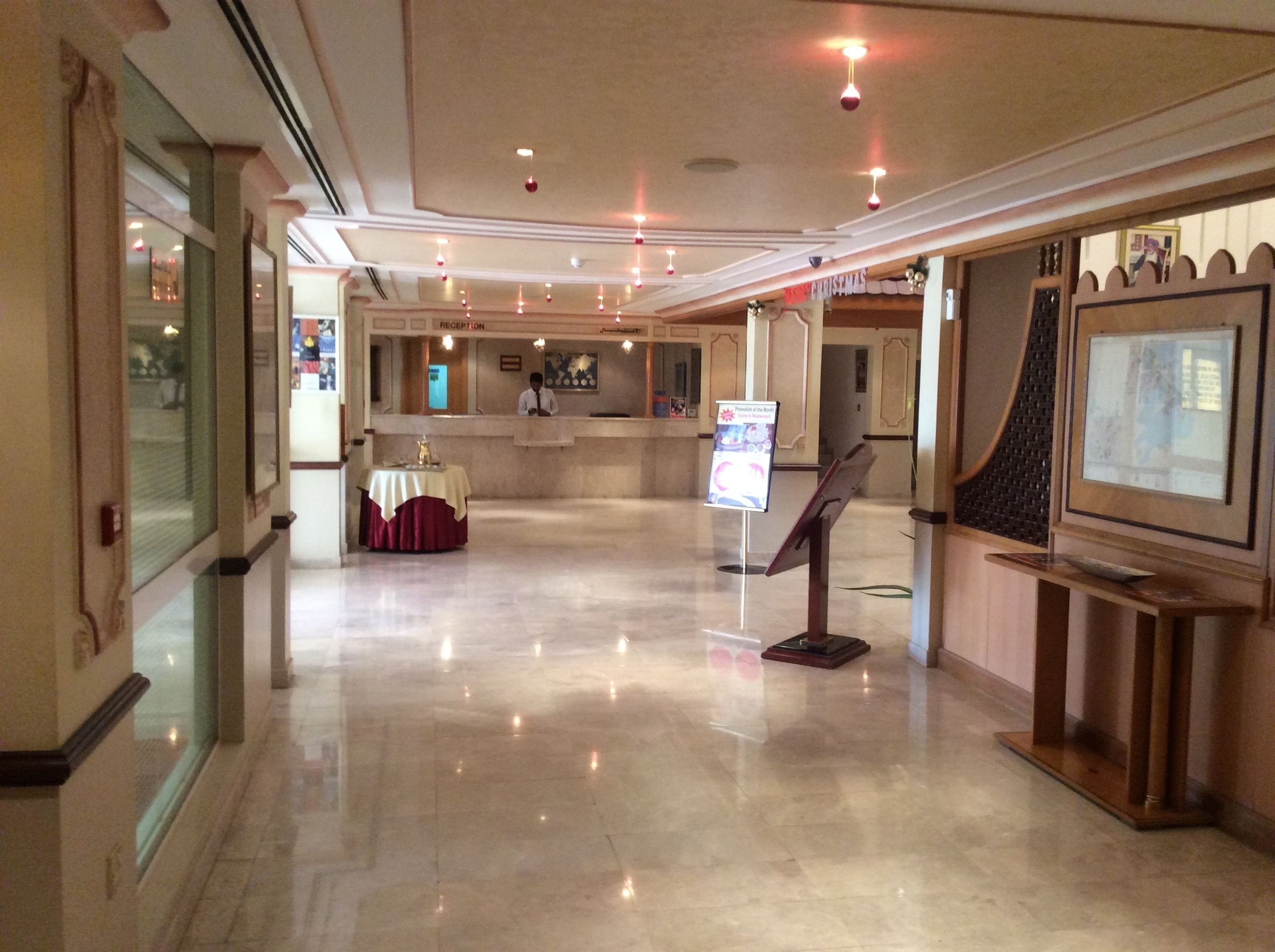 Un hall d’hôtel comprenant un comptoir d’accueil, un espace d’attente, un coin repas avec une table et des chaises, et un écran de télévision posé sur un support.