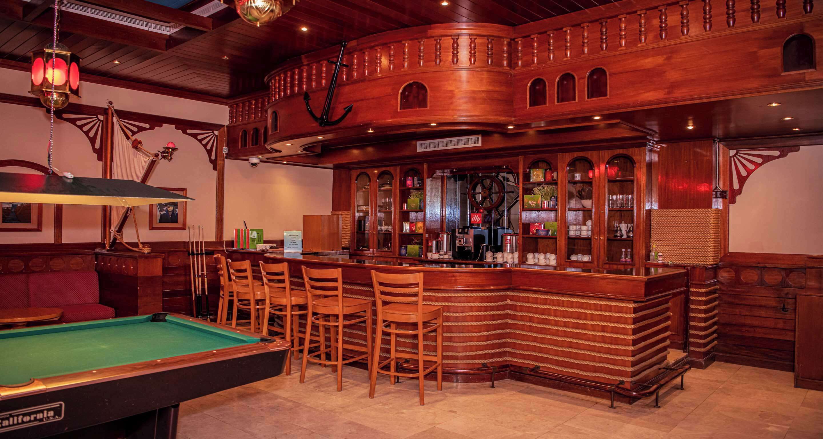 Zona de bar con mesa de billar, mostrador de madera y taburetes.