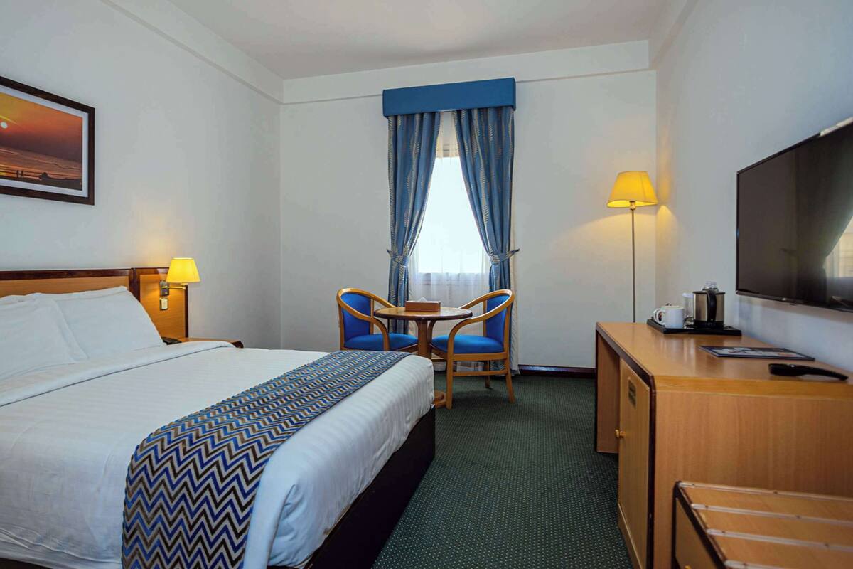 A hotel room with a bed, a desk, a chair, a television, and a painting on the wall.
