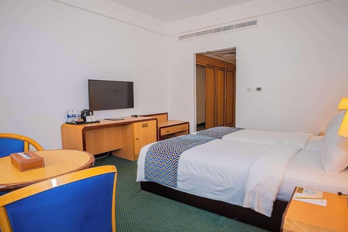 Una habitación de hotel con cama, escritorio, silla, televisión y lámpara.