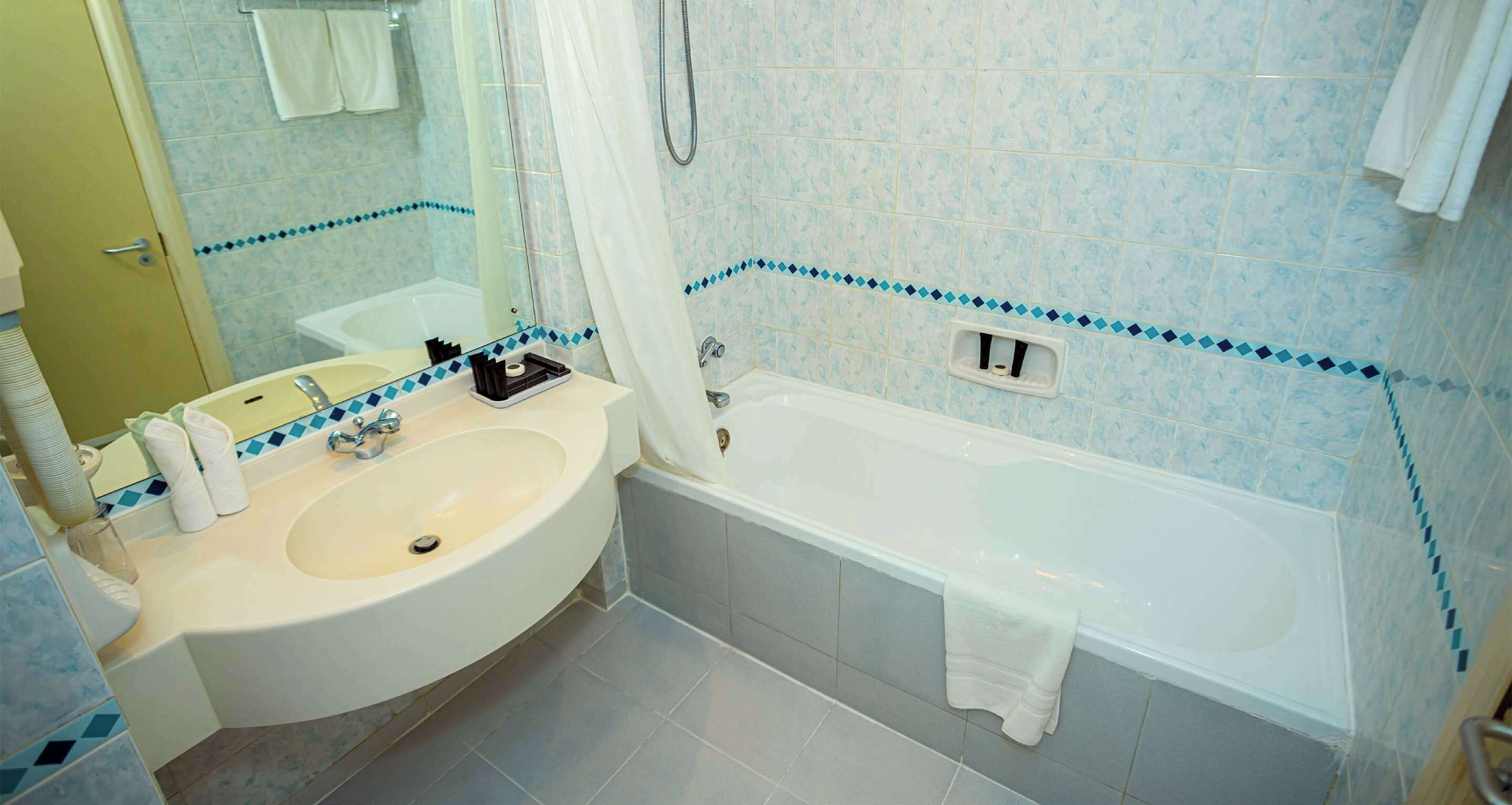 A bathroom with a sink, mirror, bathtub, and tiled walls.