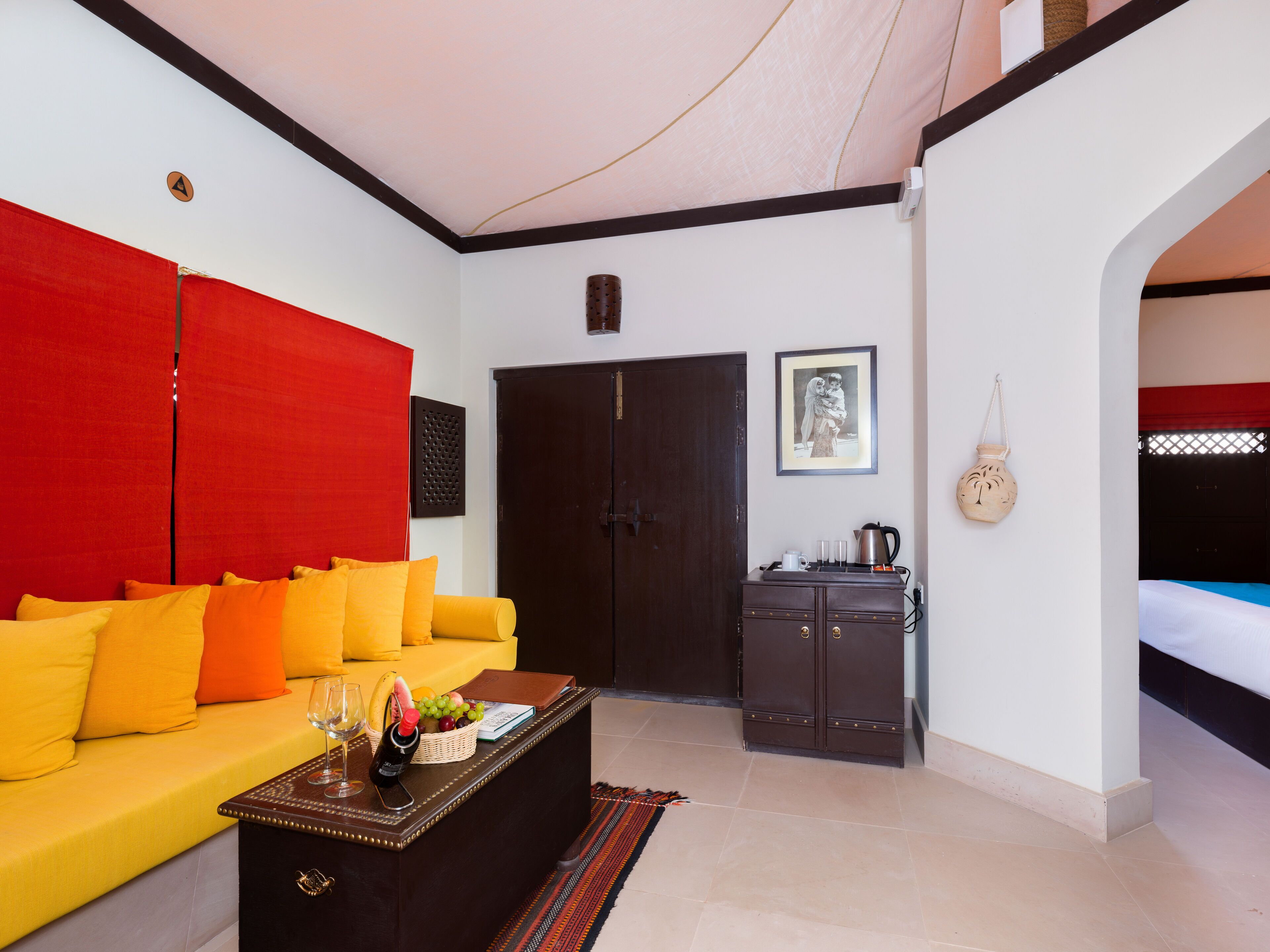 A room with a yellow sofa, a dark wooden cabinet, and a bed with a red headboard.