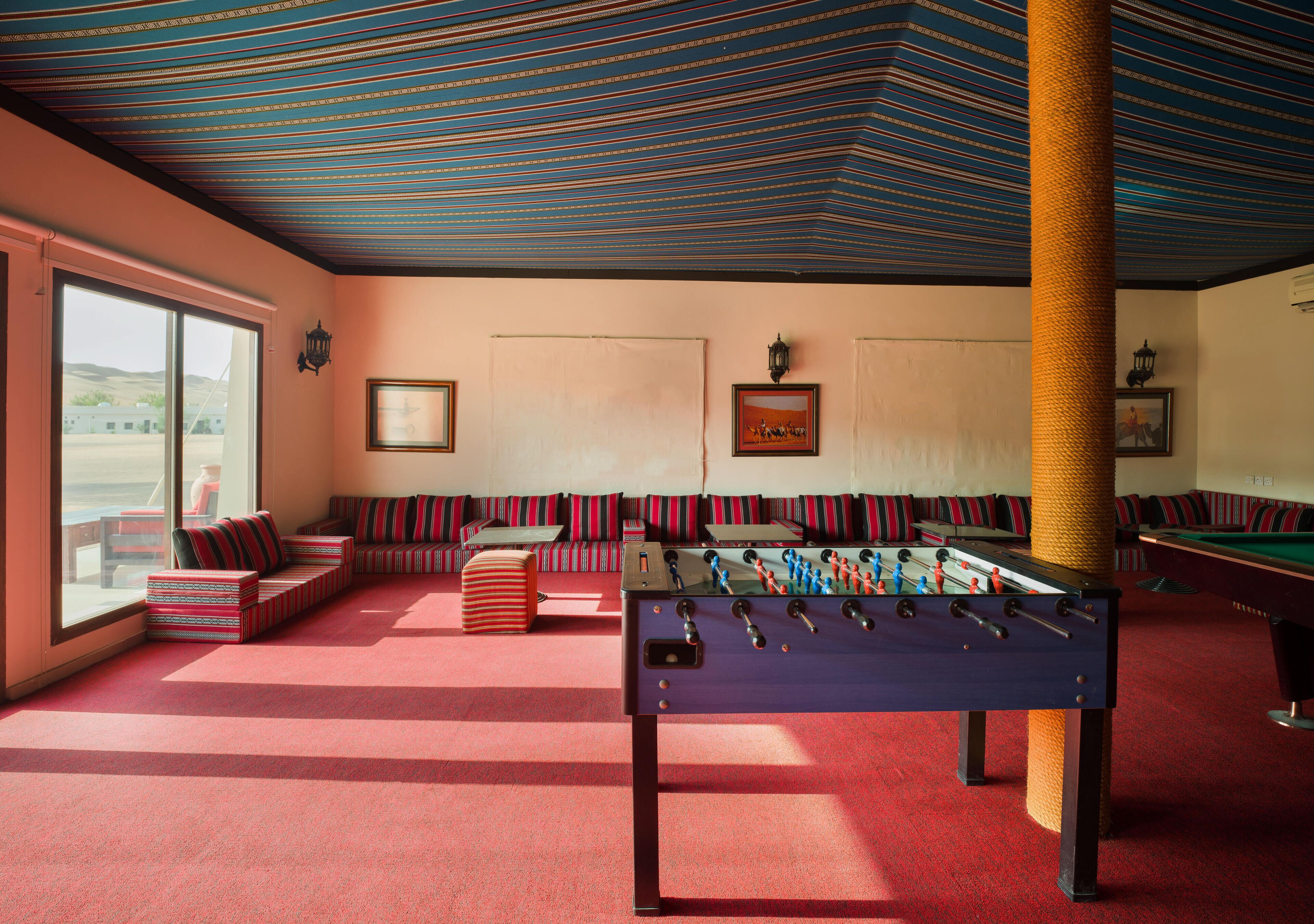 A room with a foosball table, sofas, and a billiards table.