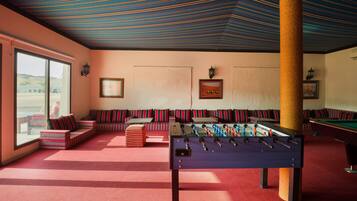 A room with a foosball table, sofas, and a billiards table.