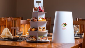 A tiered dessert display with a Desert Nights Camp logo, set on a wooden table with chairs and a wine glass. - Desert Nights Resort (Bidiya)