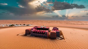 A desert landscape with a bedouin-style tent and several colorful cushions arranged on the sand. - Desert Nights Resort (Bidiya)