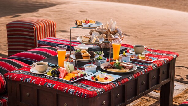 A desert picnic setup with a table set for breakfast, including plates of food, drinks, and a cup of coffee. - Desert Nights Resort (Bidiya)