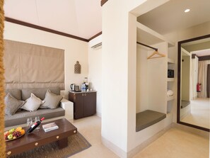 A modern hotel room with a sofa, a coffee table with fruit, a small cabinet, and a mirror.