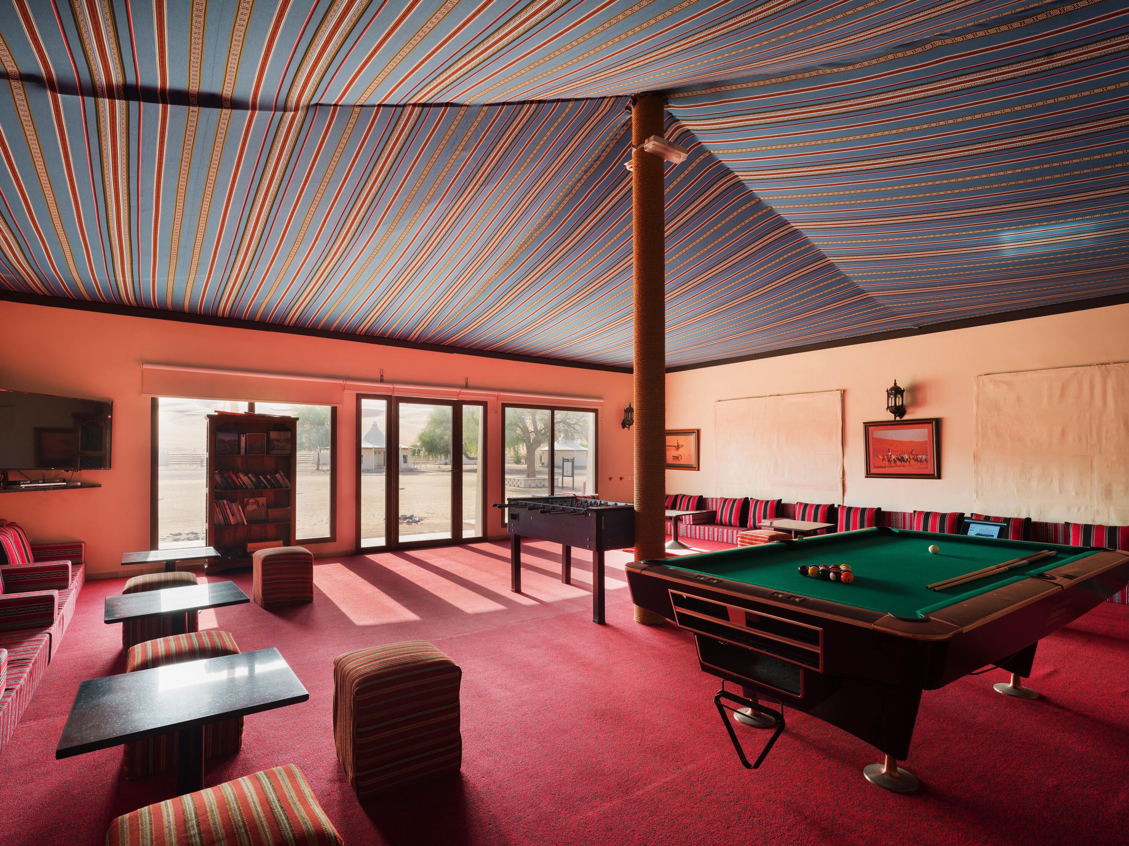 A pool table in a room with striped ceiling, red carpet, and a billiards table.
