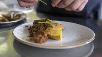 A person holding chopsticks over a plate with a piece of food and a bowl in the background.