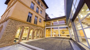 Un bâtiment doté d’une façade en pierre, de grandes fenêtres et d’une cour recouverte de gravier.