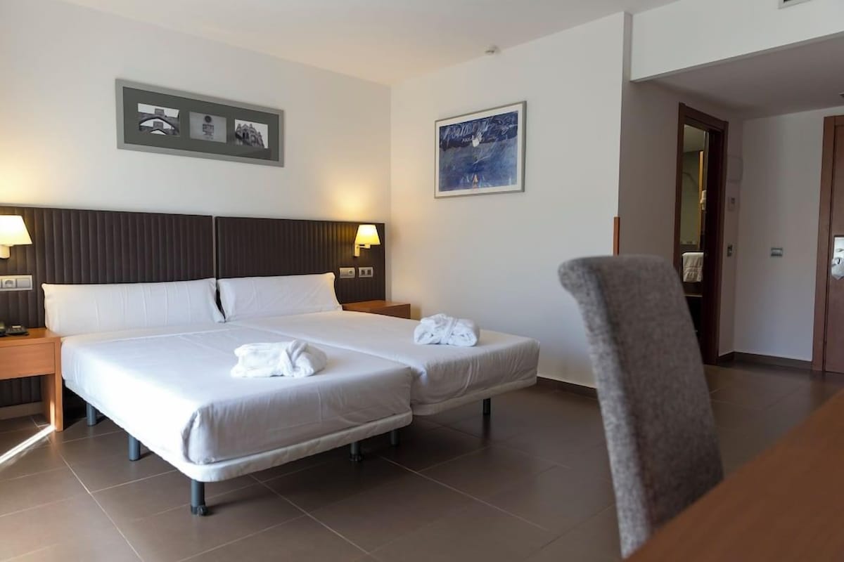 Camera d'albergo con due letti, una sedia e opere d'arte alle pareti.