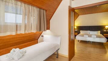 A single-bed room with wooden paneling, a window with sheer curtains, and a view into an adjacent room with a bed and nightstands.