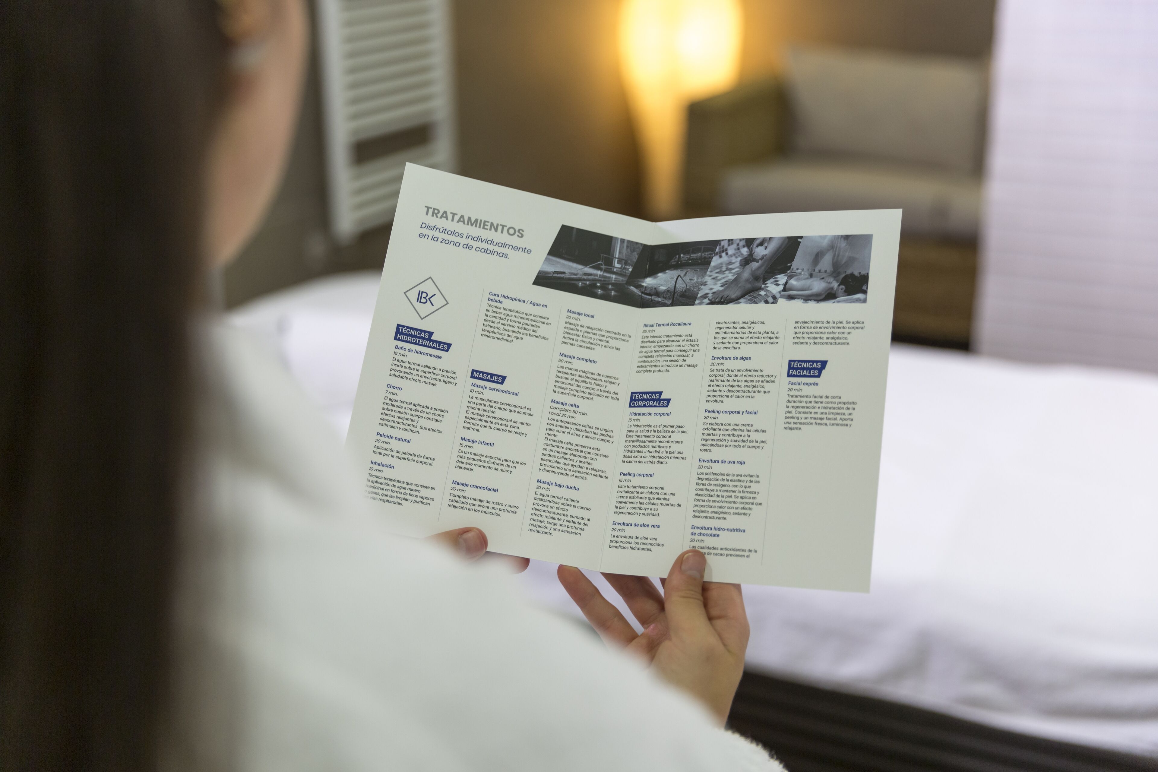 A person reading a brochure titled "TRATIMIENTOS" in a hotel room.