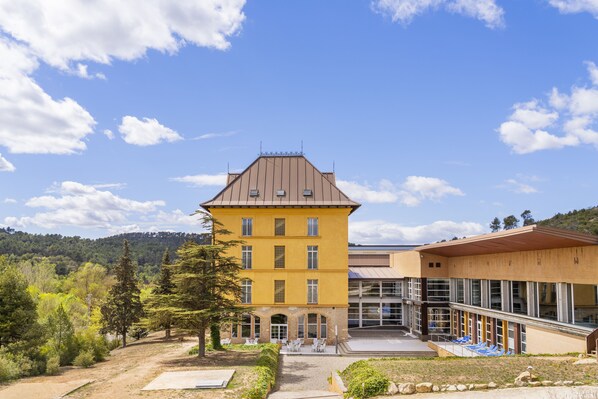 A yellow building with a large entrance and a covered area with chairs. - Iberik Hotel Balneari Rocallaura (Vallbona de les Monges)