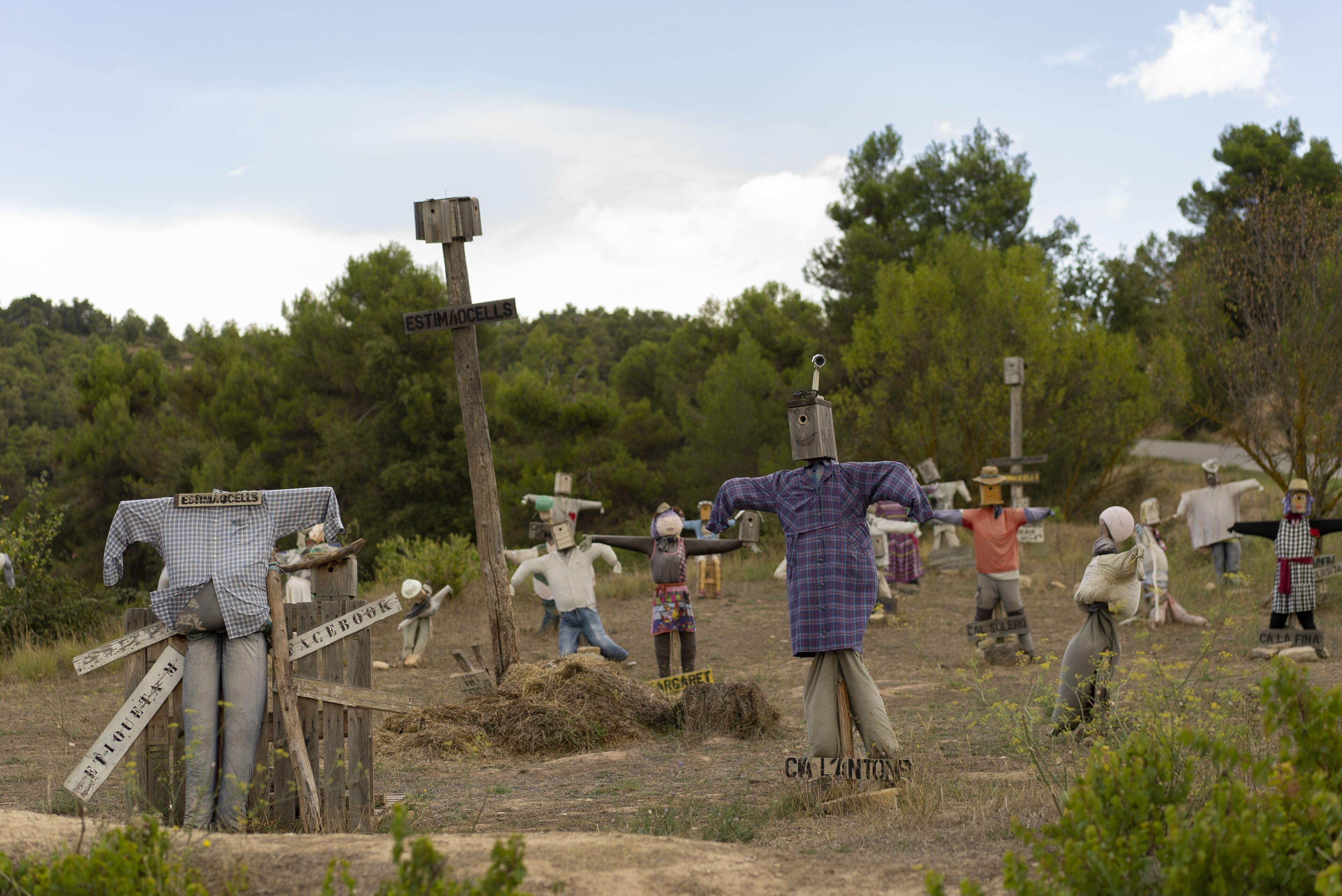 A rural outdoor scene with wooden structures and figures, including a sign that reads "ESTIMACELLES".
