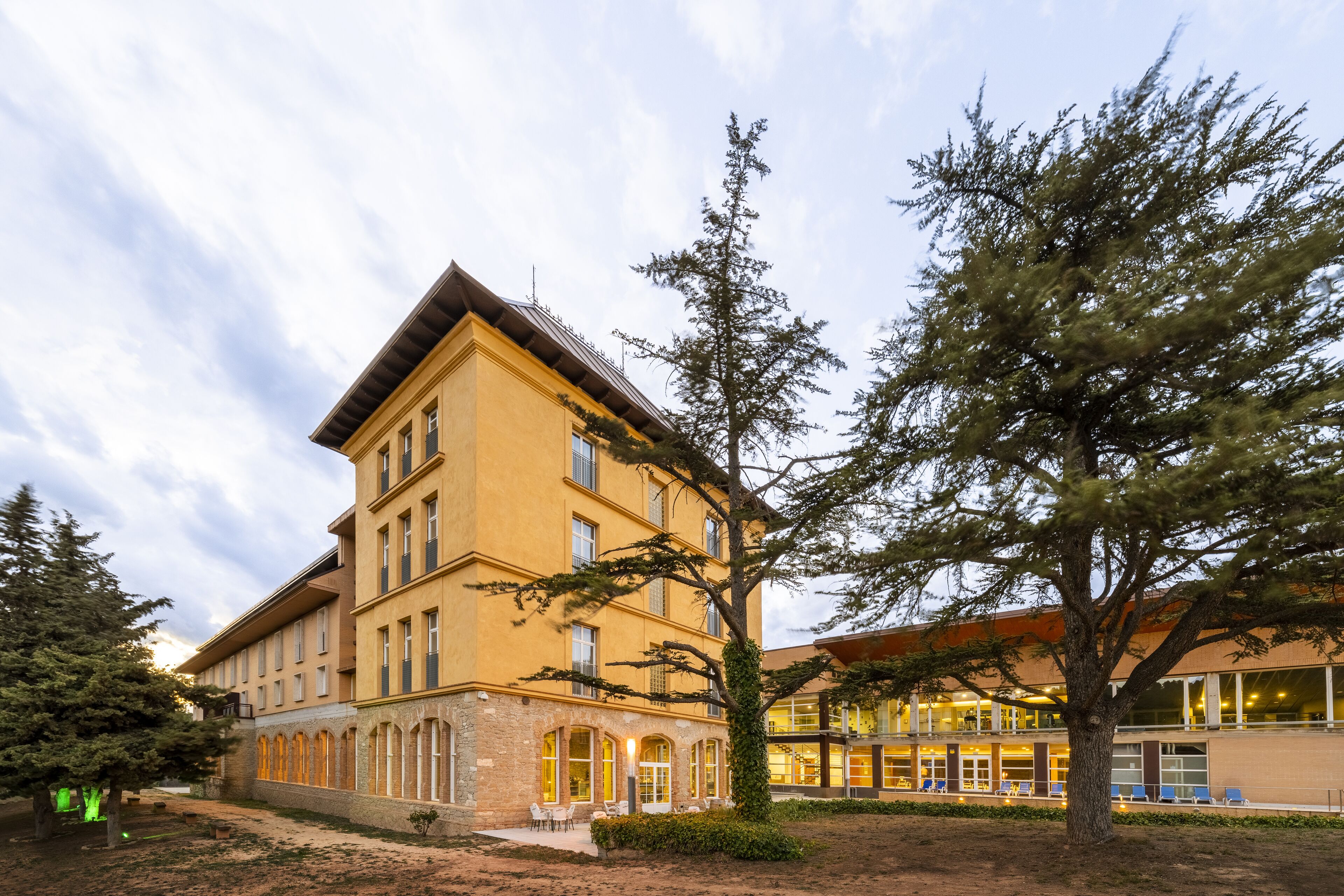 Ein mehrstöckiges Gebäude mit gelber Fassade, großen Fenstern und einem Innenhof mit Außenbestuhlung.