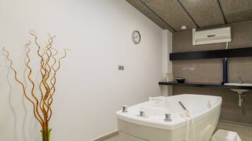 Un baño moderno con una bañera independiente, un reloj de pared y una planta decorativa.