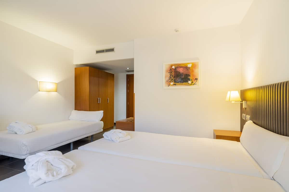 Een hotelkamer met twee bedden, een houten garderobe en een schilderij aan de muur.
