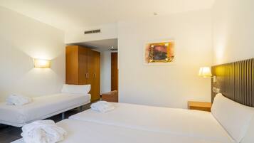 Een hotelkamer met twee bedden, een houten garderobe en een schilderij aan de muur.