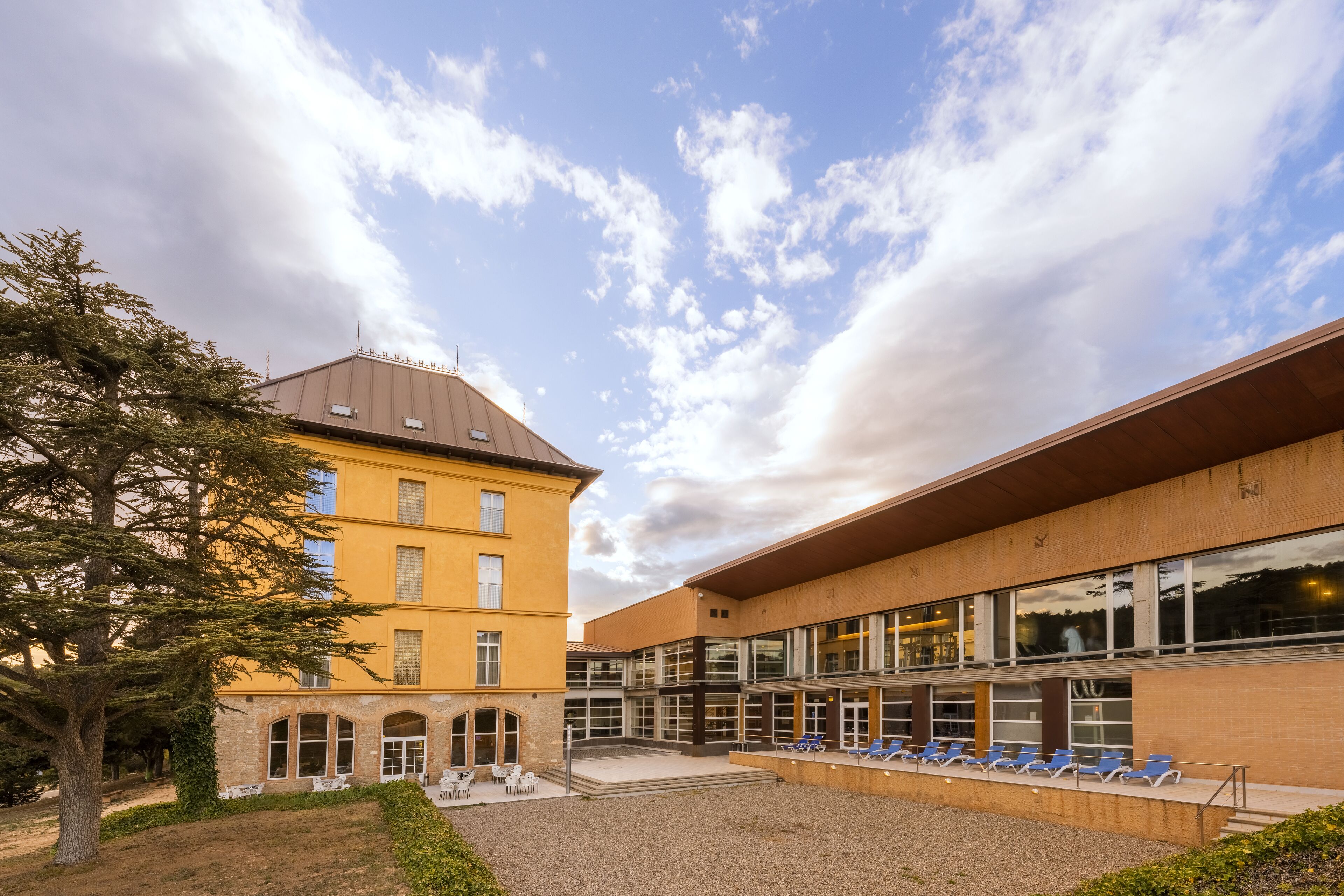 Ein Gebäude mit Innenhof, einem Baum und einer Reihe blauer Stühle.