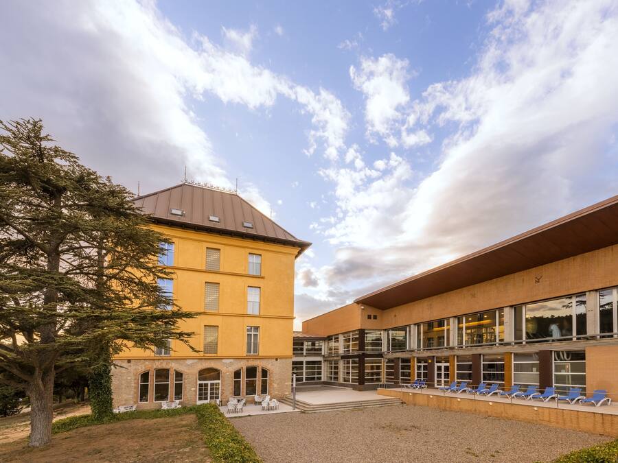 Ein Gebäude mit Innenhof, einem Baum und einer Reihe blauer Stühle.