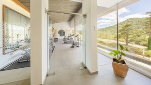 Une salle de sport moderne équipée de matériel d’exercice, dotée de grandes fenêtres et offrant une vue sur une zone boisée.