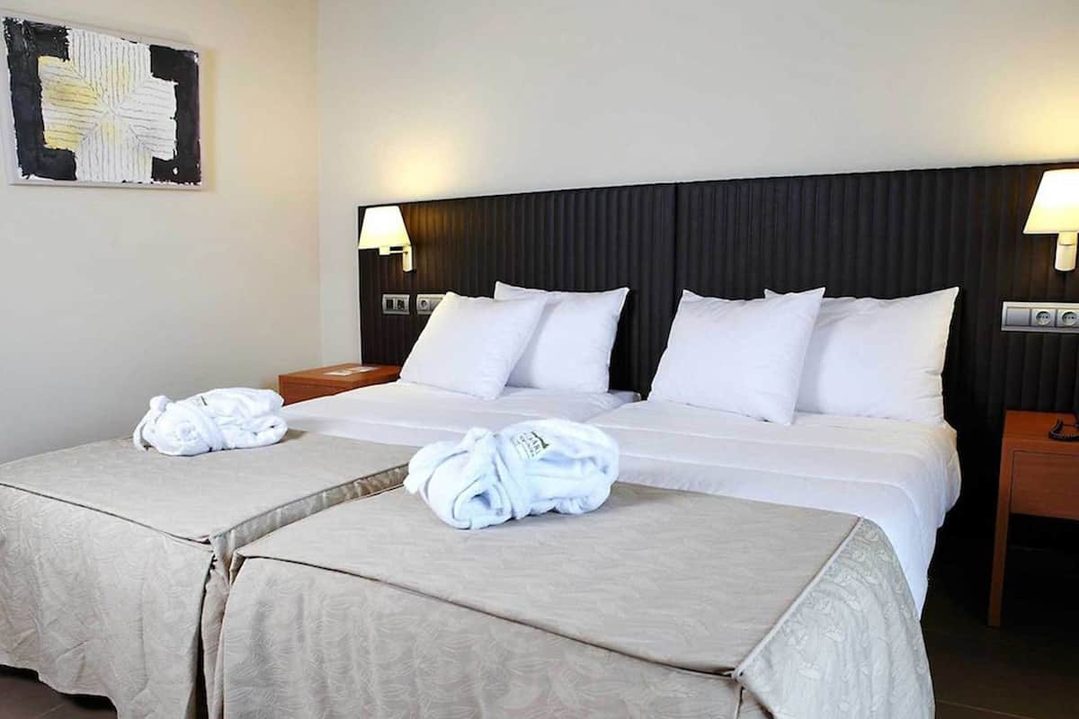 Hotelkamer met twee bedden, wit beddengoed, een hoofdbord, bedlampjes en een aan de muur bevestigd kunstwerk.