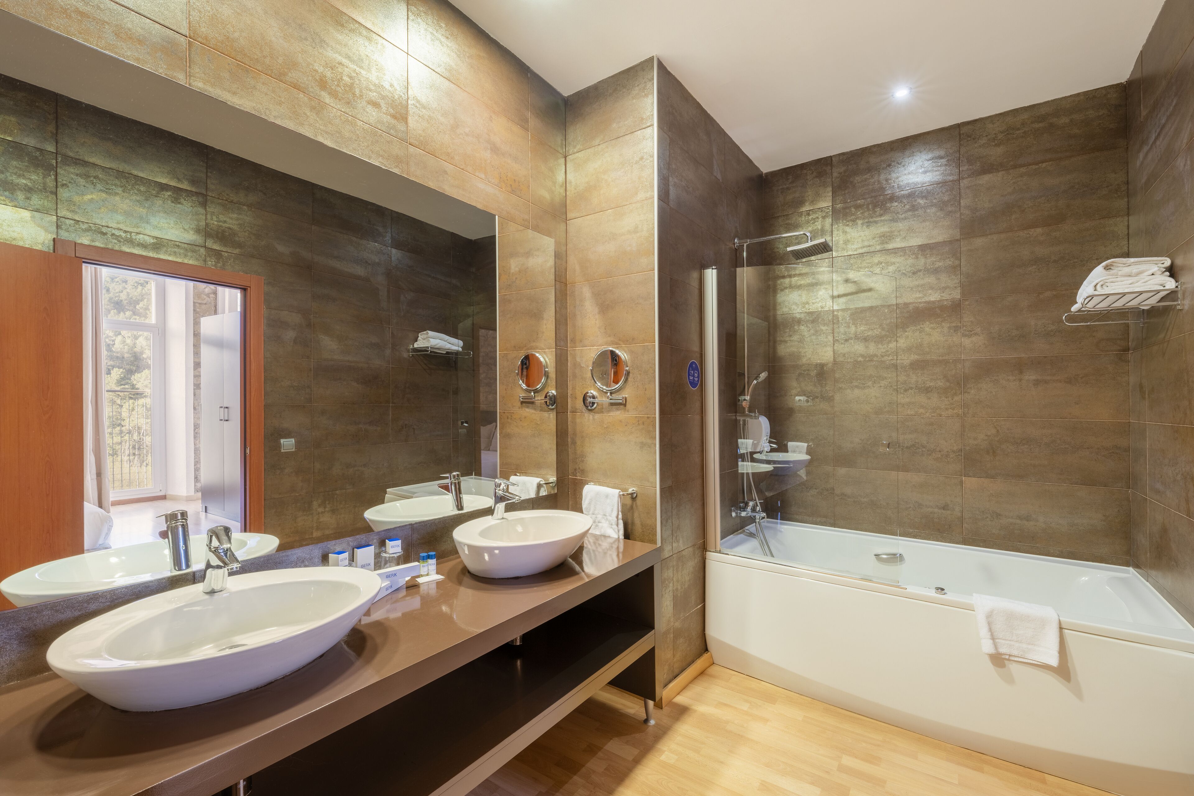 A modern bathroom with two sinks, a large mirror, a bathtub, and a shower area.