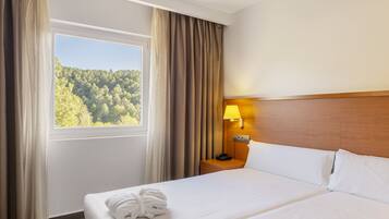 Une chambre d’hôtel avec un lit, une table de chevet avec une lampe et une fenêtre avec des rideaux.