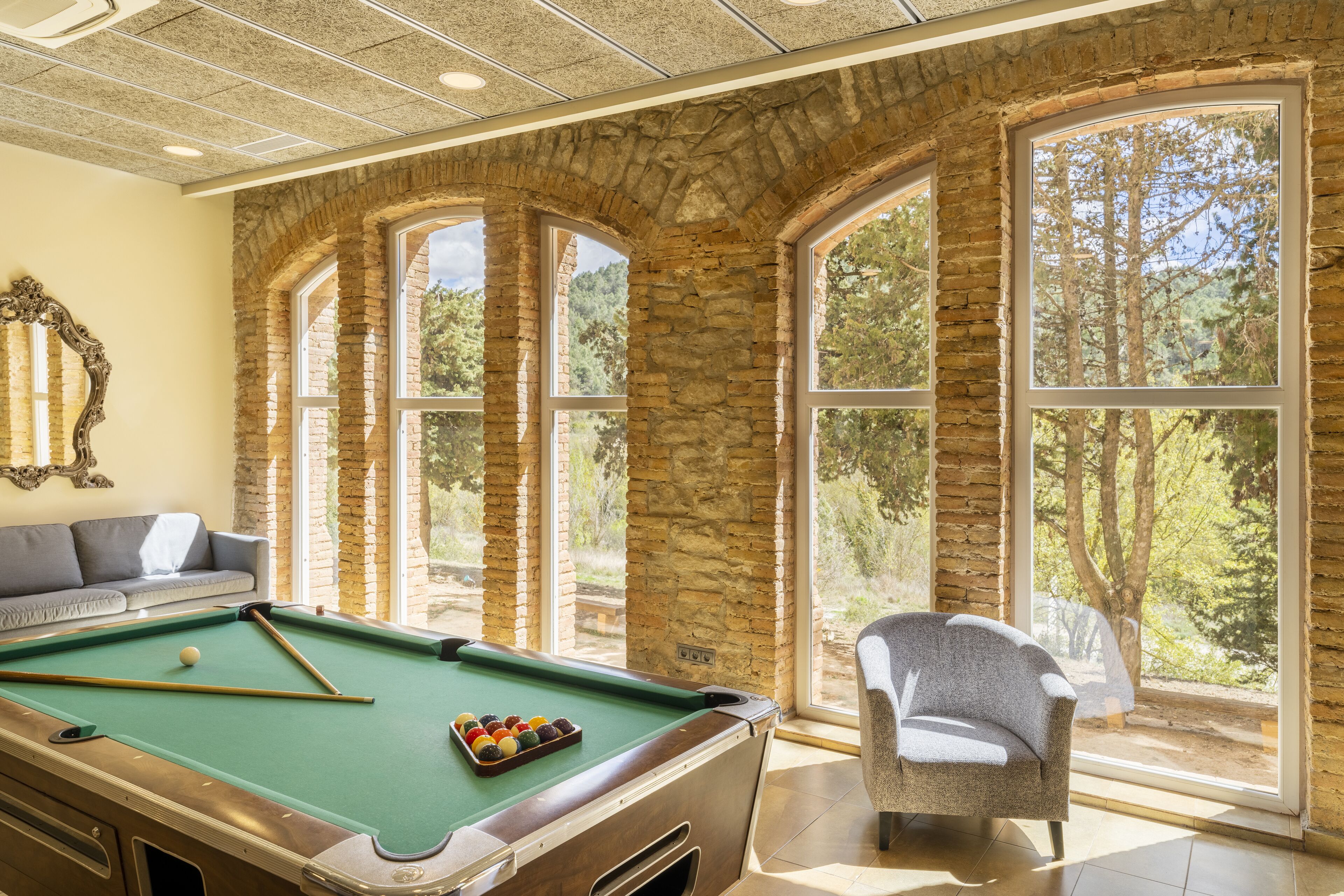 Una mesa de billar en una habitación con paredes de piedra y ventanas grandes.