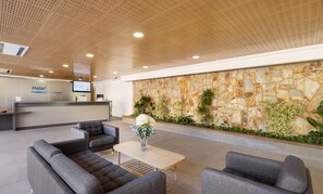 A modern hotel lobby with a reception desk, grey sofas, a coffee table, and a stone wall with plants. - Iberik Hotel Balneari Rocallaura (Vallbona de les Monges)