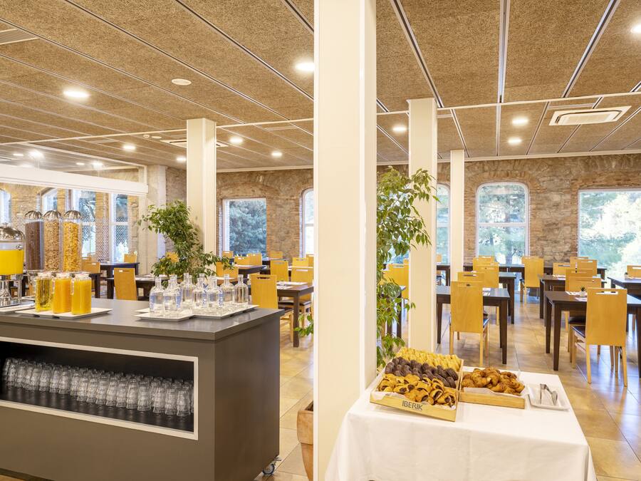 A spacious dining area with high ceilings, large windows, and a buffet setup with various food items and beverages.