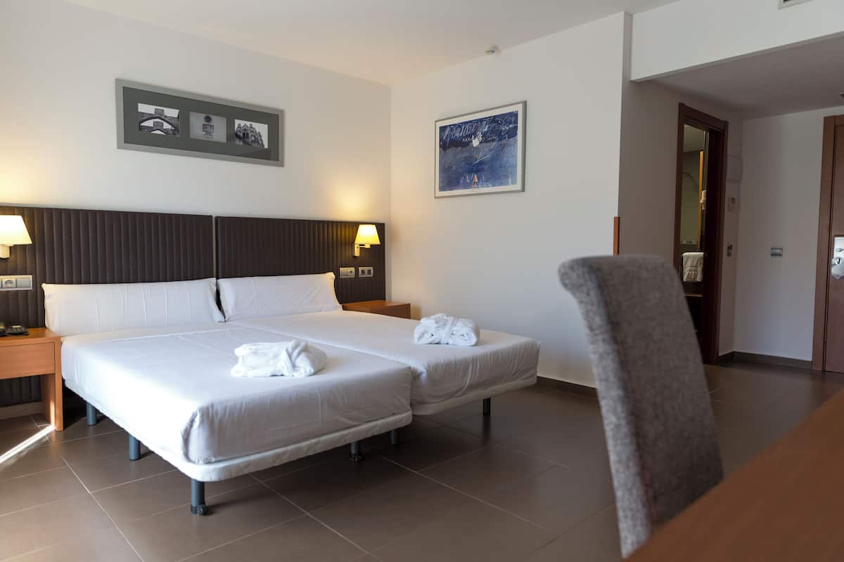 Een hotelkamer met een groot bed, twee nachtkastjes, een stoel en kunstwerken aan de wanden.