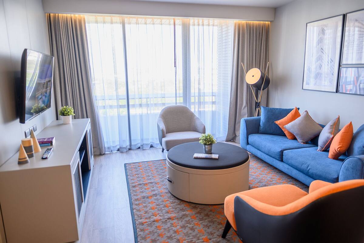 Une chambre d’hôtel moderne avec un canapé, un fauteuil et une table basse ronde agrémentée d’une plante.