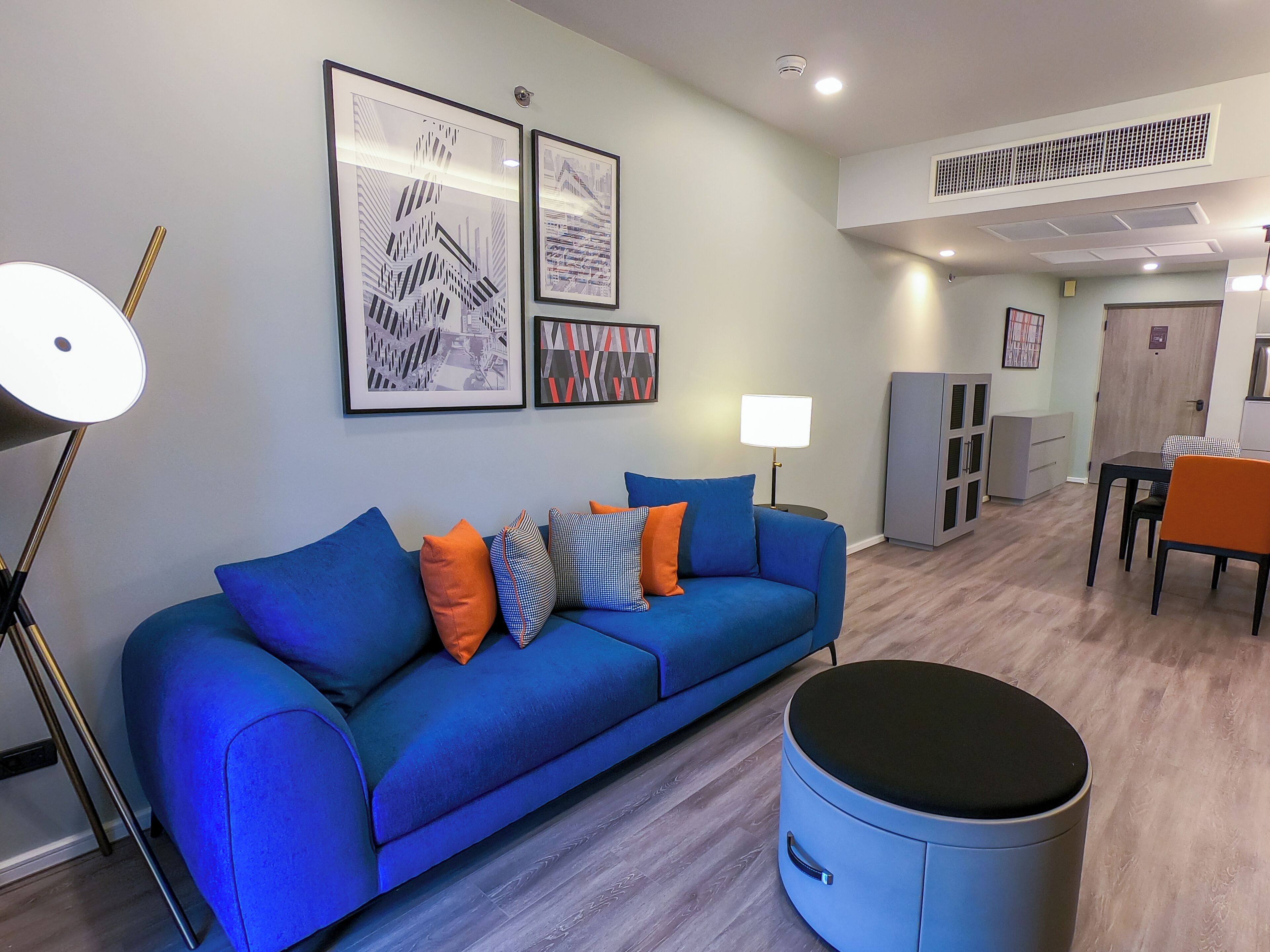 Un salon moderne avec un canapé bleu, un pouf rond et un coin repas comprenant une table et des chaises.