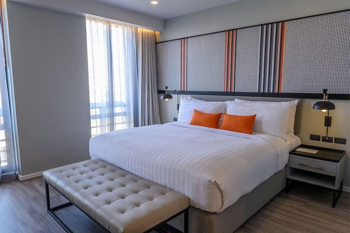 A modern hotel room with a large bed, a bench, a nightstand, and a wall with a textured pattern.