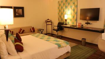Habitación de hotel con cama, escritorio, silla, televisor y lámpara.