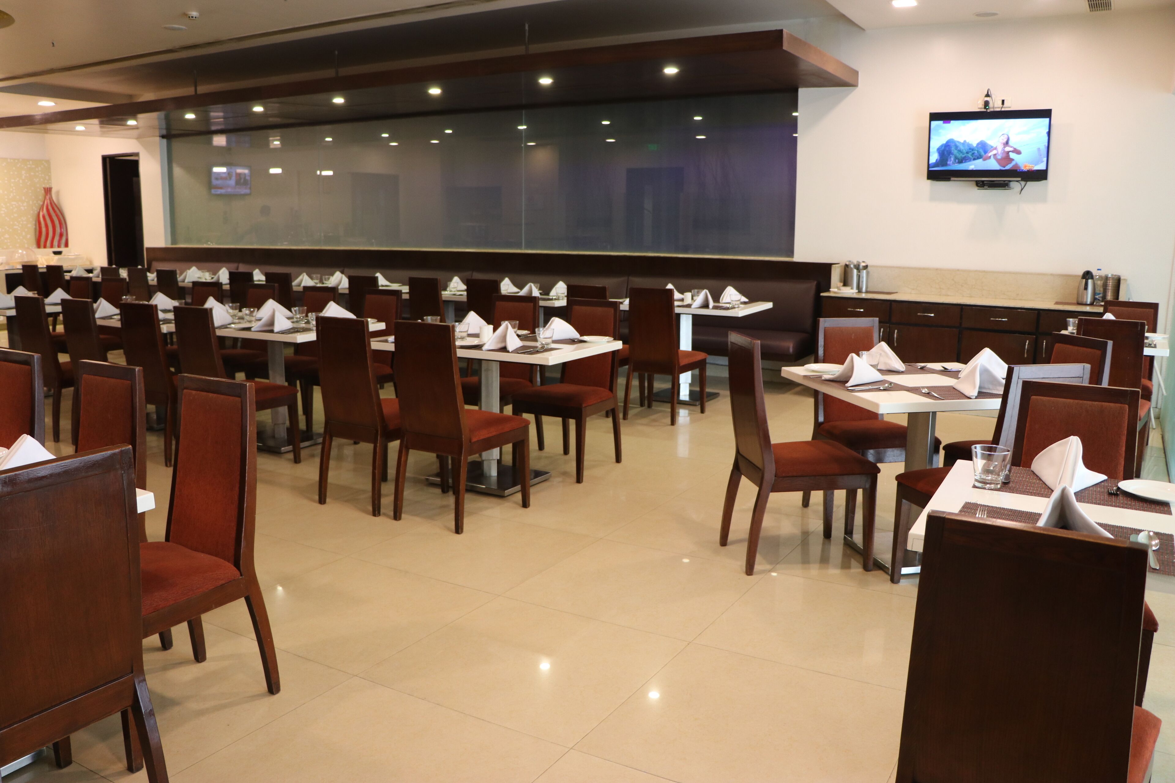A spacious dining area with multiple tables and chairs, a large window, and a television mounted on the wall.