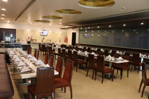 A spacious restaurant with long tables and chairs, a television screen, and a large window.