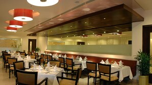 A restaurant with multiple tables set for dining, featuring a modern interior with a large mirror and red pendant lighting. - Fortune Inn Sree Kanya, Visakhapatnam - Member ITC Hotels' Group (Visakhapatnam)