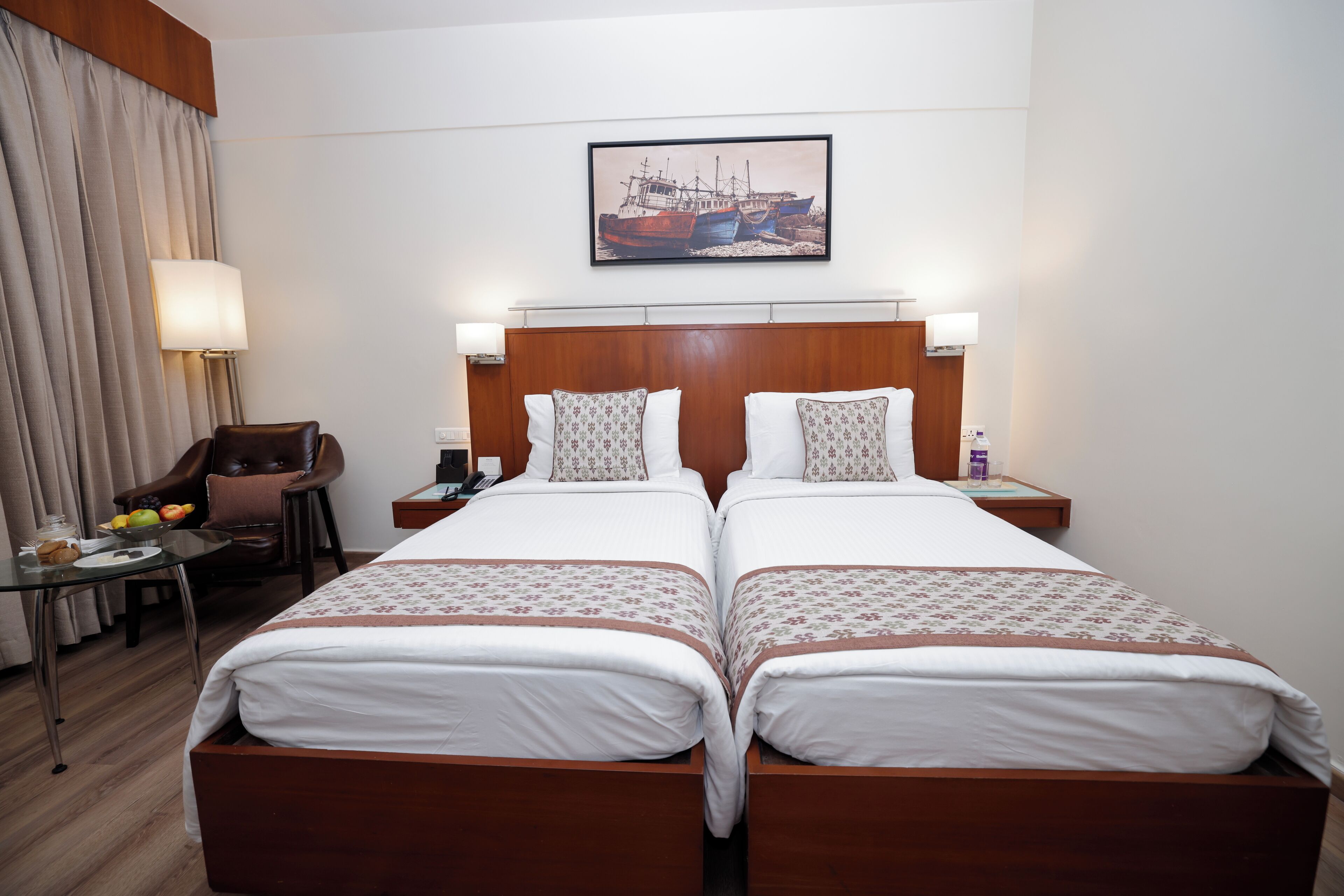 Habitación de hotel con dos camas, cabecero de madera, escritorio con silla, lámpara y un cuadro en la pared.