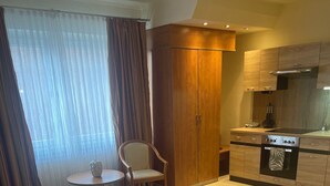 A hotel room with a bed, a small table with a chair, a kitchenette, and a large window with curtains. - Hotel Falk (Bremen)